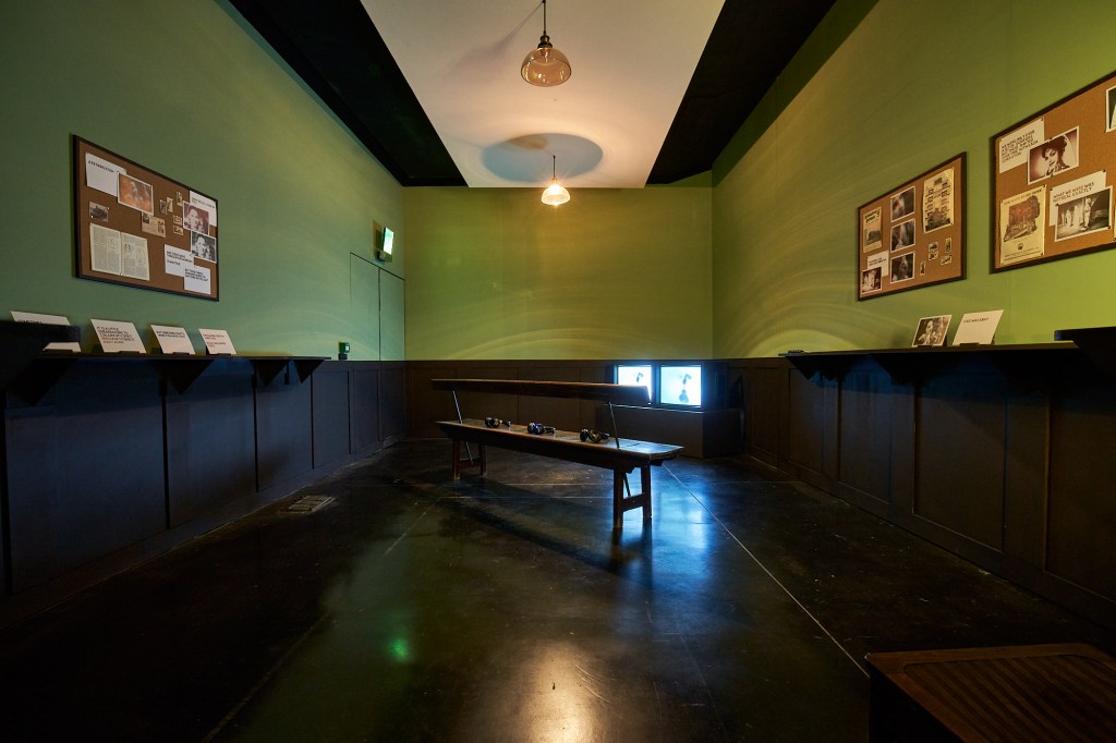 Installation view of Dark Circles at FACT Liverpool, showing two TV screens and viewing bench.