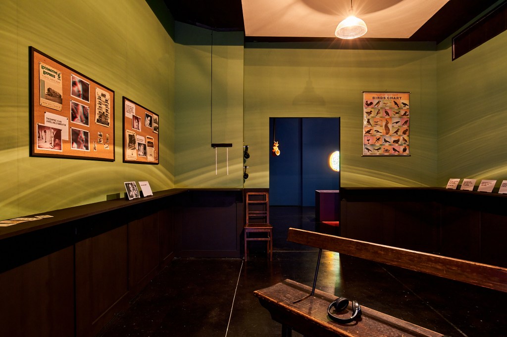 Installation view of Dark Circles at FACT Liverpool, showing cork boards, viewing bench, headphones, posters and ephemera.